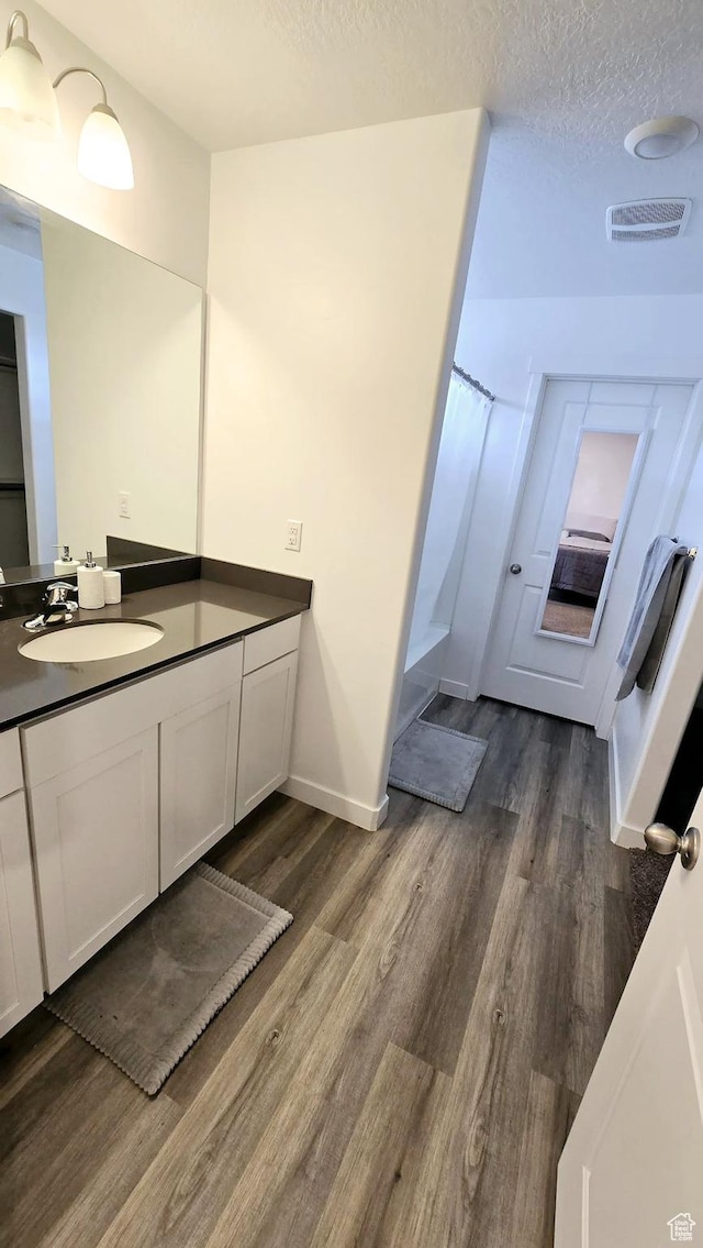 bathroom with wood-type flooring, vanity, a textured ceiling, and walk in shower