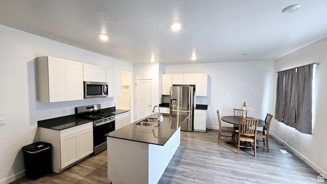 kitchen with appliances with stainless steel finishes, sink, white cabinets, light hardwood / wood-style floors, and a center island with sink