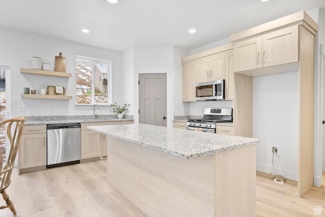 kitchen featuring light wood-style floors, a kitchen island, light stone counters, a sink, and stainless steel appliances