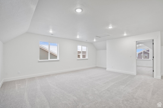 empty room with baseboards, a textured ceiling, light carpet, and lofted ceiling