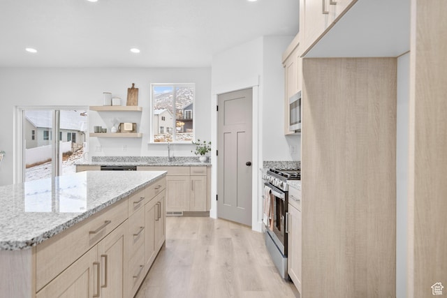 kitchen featuring light brown cabinets, a sink, appliances with stainless steel finishes, light wood-style floors, and light stone countertops