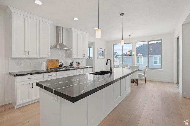 kitchen featuring wall chimney exhaust hood, sink, an island with sink, and white cabinets