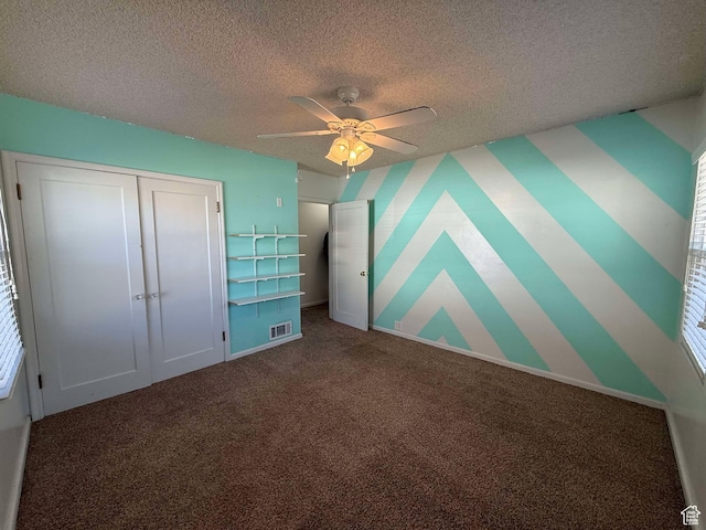 unfurnished bedroom with ceiling fan, a closet, a textured ceiling, and dark colored carpet