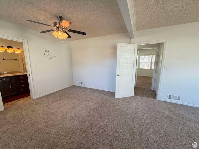 unfurnished bedroom with ceiling fan, ensuite bathroom, light carpet, and a textured ceiling