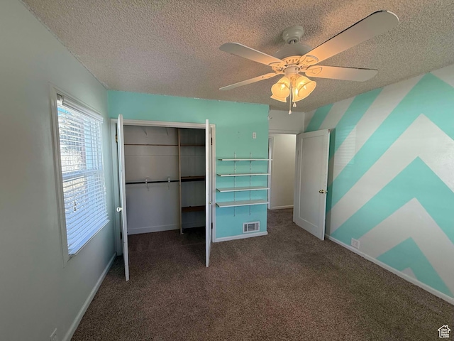 unfurnished bedroom with ceiling fan, a textured ceiling, dark carpet, and a closet