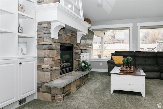 living room with a stone fireplace and dark colored carpet