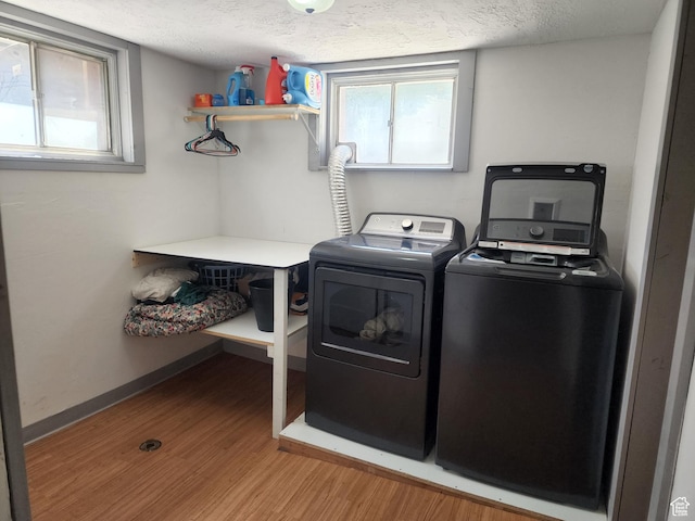 clothes washing area with light wood finished floors, independent washer and dryer, a textured ceiling, and a healthy amount of sunlight