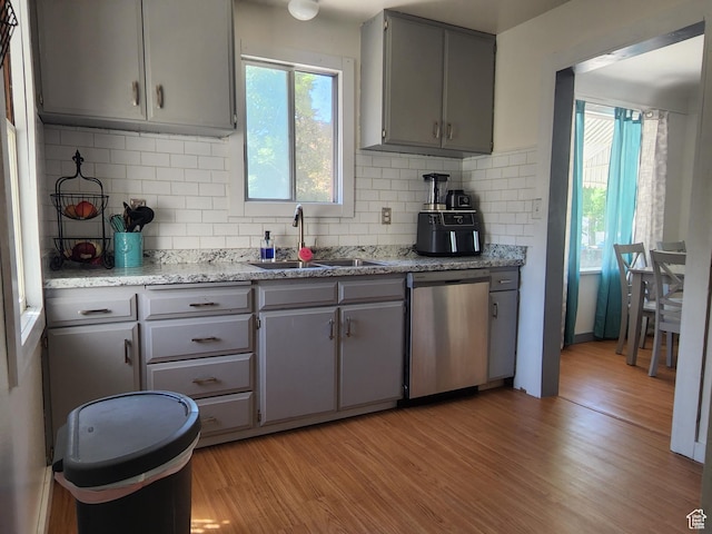 kitchen with light wood-style flooring, plenty of natural light, a sink, gray cabinets, and stainless steel dishwasher