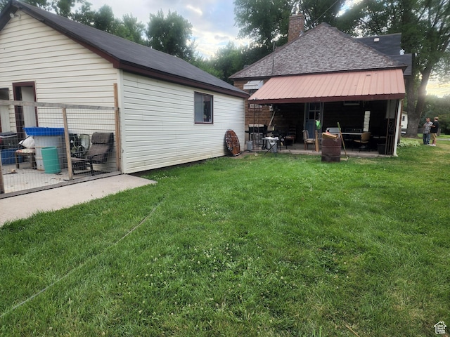 rear view of house featuring a yard, a chimney, roof with shingles, and a patio area