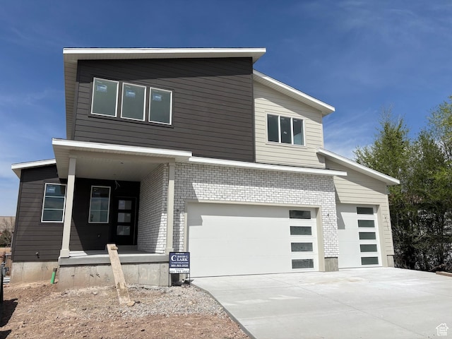 modern home featuring concrete driveway, a garage, covered porch, and brick siding