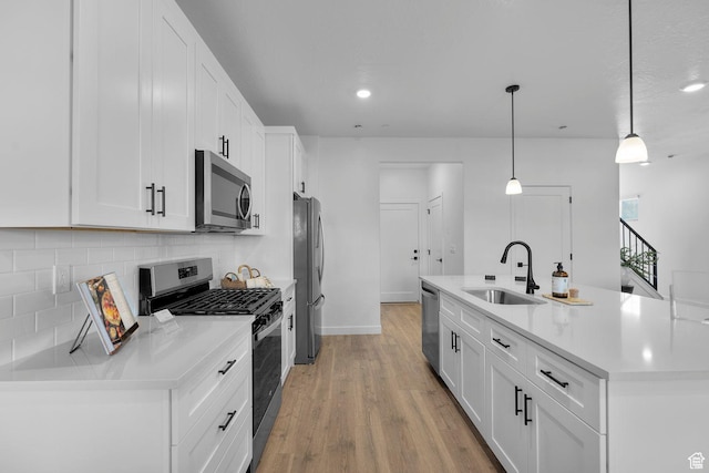 kitchen with backsplash, white cabinets, a kitchen island with sink, appliances with stainless steel finishes, and a sink