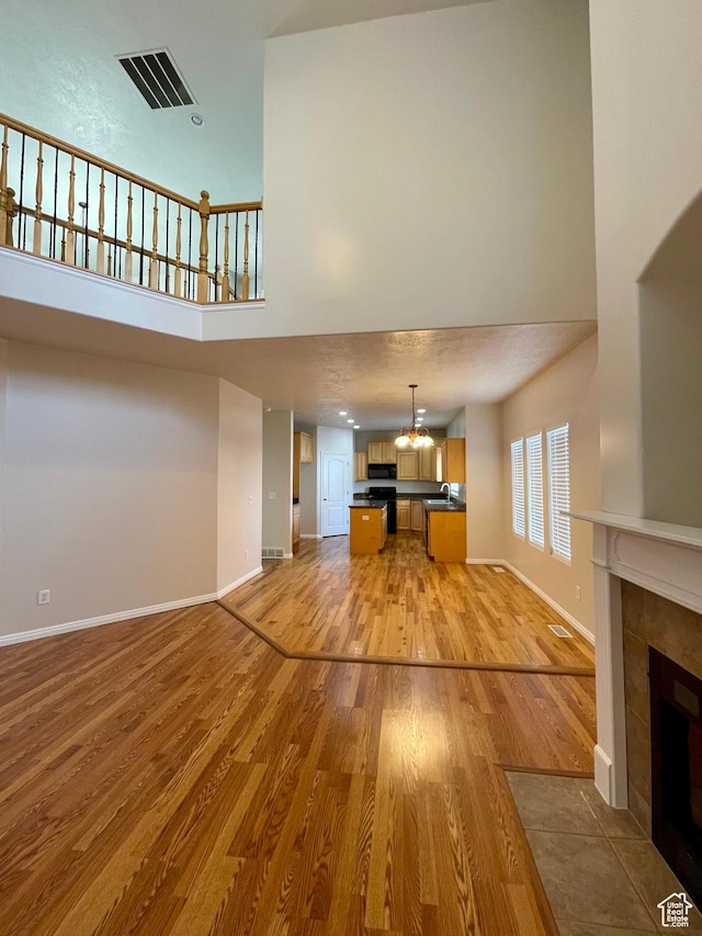 909 E Rosebud Ct, Draper, UT 84020 - unfurnished living room with a tiled fireplace, light hardwood / wood-style flooring, and a high ceiling