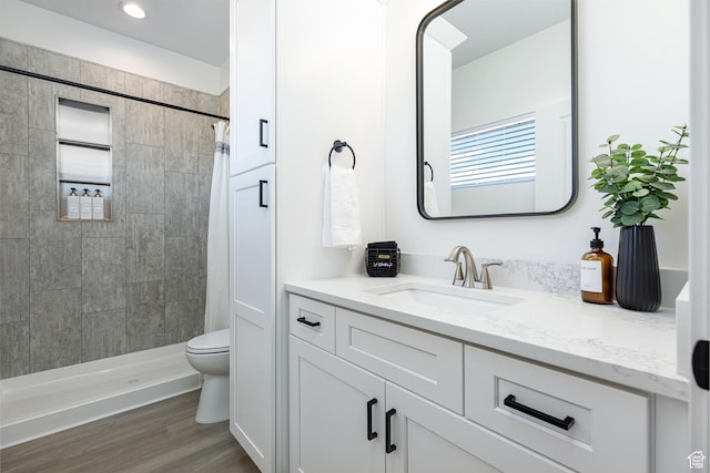 bathroom featuring a tile shower, toilet, vanity, and wood finished floors