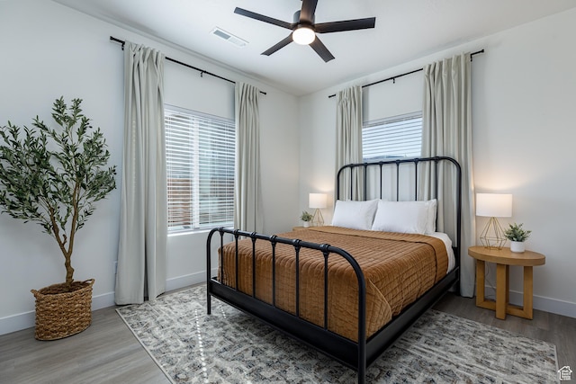 bedroom featuring baseboards, multiple windows, wood finished floors, and visible vents