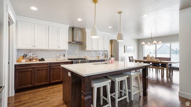 kitchen featuring wall chimney range hood, a sink, range, tasteful backsplash, and an island with sink