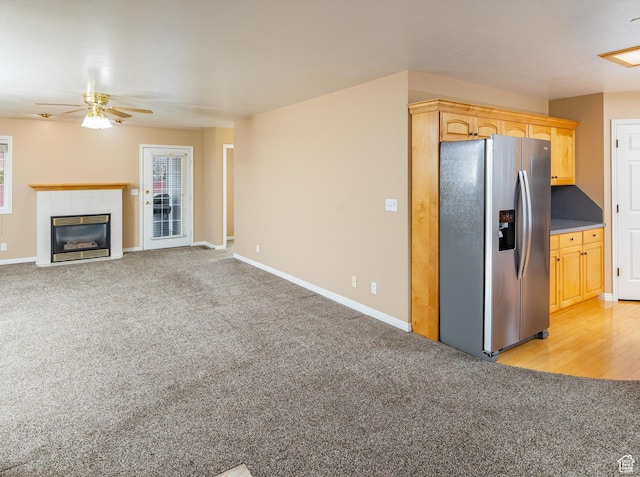 kitchen with ceiling fan, stainless steel refrigerator with ice dispenser, a fireplace, light brown cabinetry, and light colored carpet