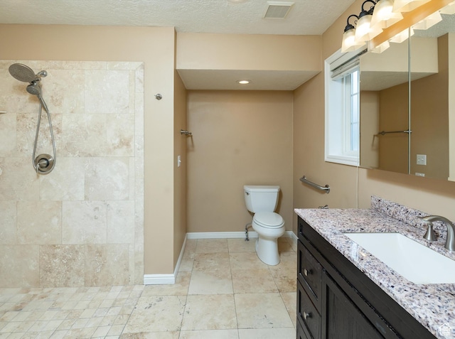 bathroom featuring toilet, a textured ceiling, a tile shower, vanity, and tile patterned flooring