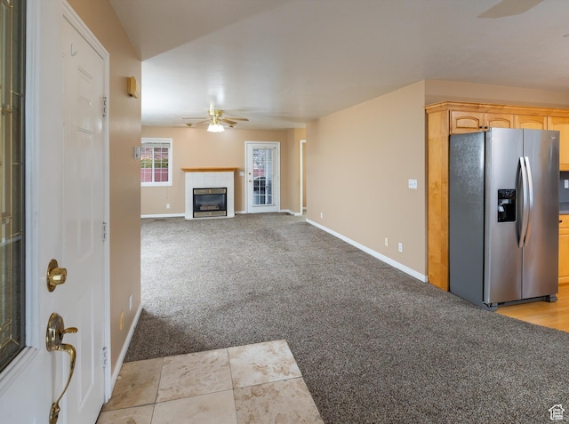 unfurnished living room featuring ceiling fan, light colored carpet, and a tiled fireplace