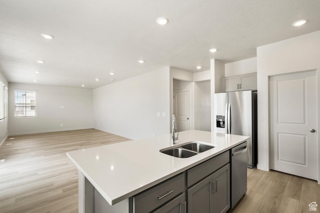 kitchen featuring a sink, gray cabinets, stainless steel appliances, light wood finished floors, and a center island with sink