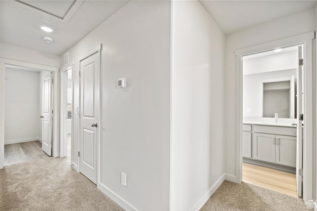 corridor with light colored carpet, baseboards, and a sink