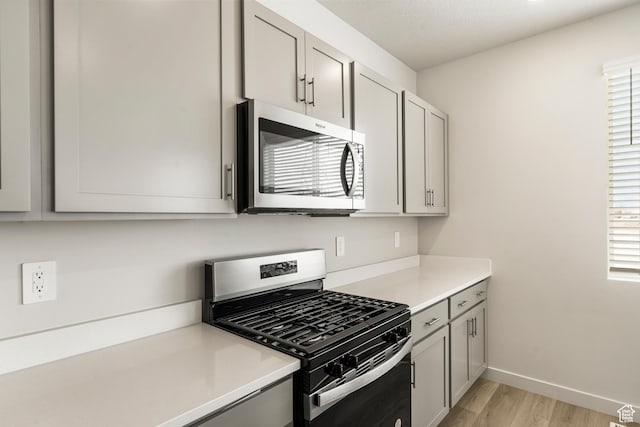 kitchen with stainless steel appliances, gray cabinetry, light wood-style flooring, and light countertops