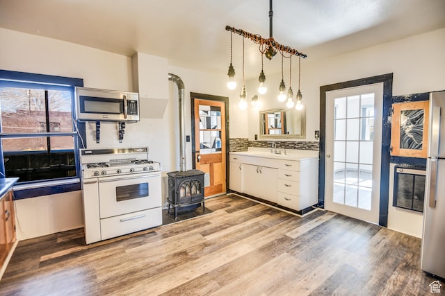 kitchen with appliances with stainless steel finishes, white cabinetry, hanging light fixtures, tasteful backsplash, and light wood-type flooring