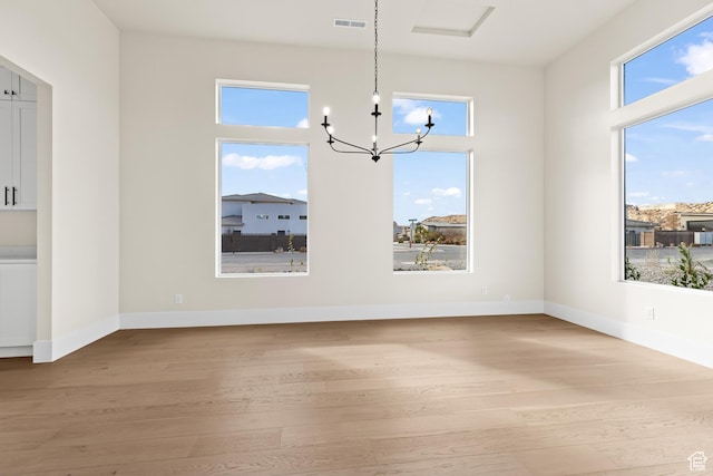 unfurnished dining area featuring an inviting chandelier and light hardwood / wood-style flooring