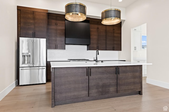 kitchen with dark brown cabinets, light hardwood / wood-style flooring, high quality fridge, and a center island with sink