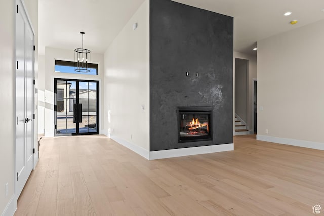 interior space with french doors, a notable chandelier, a fireplace, and light hardwood / wood-style flooring