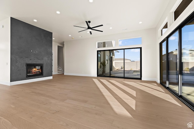 unfurnished living room with ceiling fan, a large fireplace, and light hardwood / wood-style floors