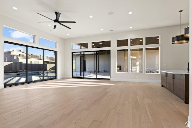unfurnished living room with a high ceiling, ceiling fan, and light hardwood / wood-style floors
