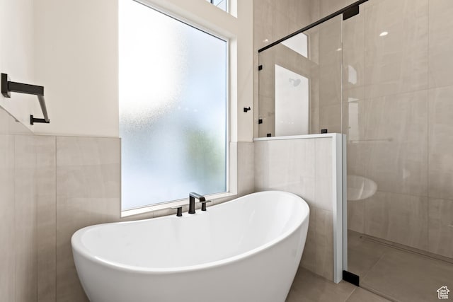bathroom featuring plus walk in shower, tile patterned flooring, tile walls, and a wealth of natural light