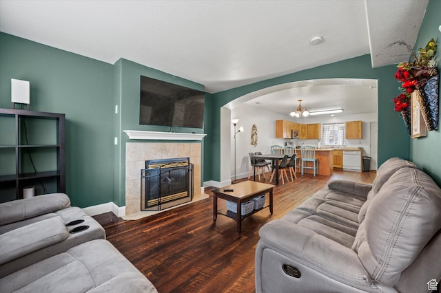 living room featuring arched walkways, a tiled fireplace, an inviting chandelier, wood finished floors, and baseboards