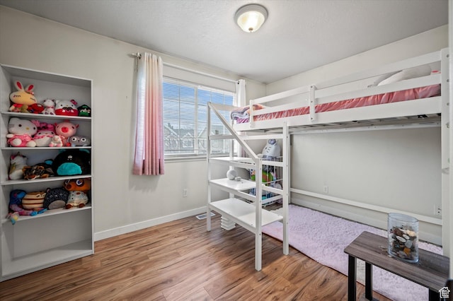 bedroom with a textured ceiling, wood finished floors, and baseboards