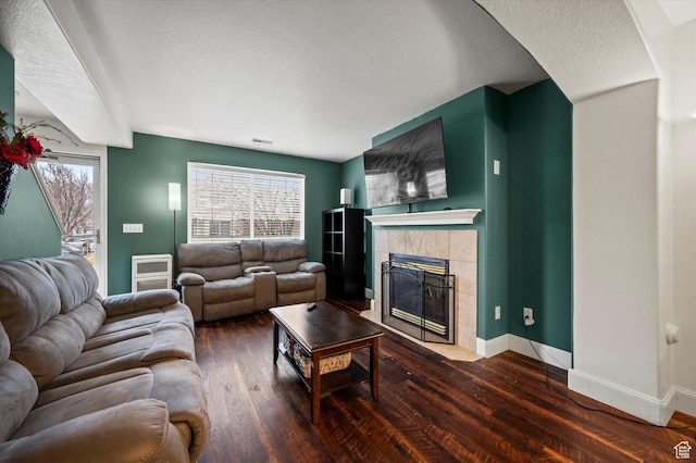 living room with a fireplace, visible vents, a textured ceiling, wood finished floors, and baseboards