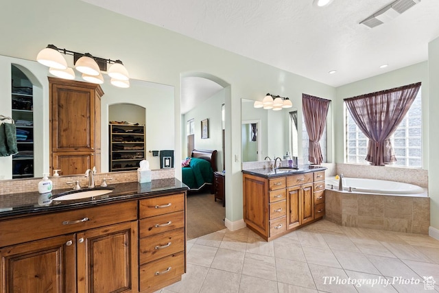 bathroom with a relaxing tiled tub, vanity, tile patterned flooring, and decorative backsplash