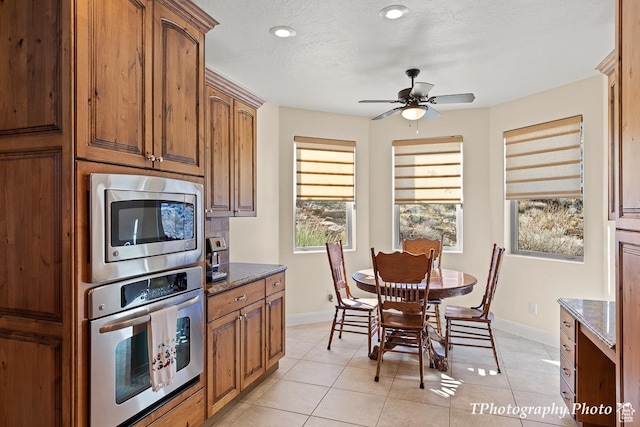 kitchen with light tile patterned flooring, dark stone counters, ceiling fan, stainless steel appliances, and a textured ceiling