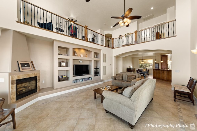 tiled living room featuring a tiled fireplace, built in features, ceiling fan, and a high ceiling