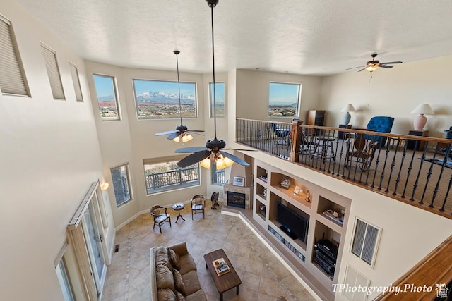 living room featuring built in shelves, ceiling fan, a textured ceiling, and a towering ceiling