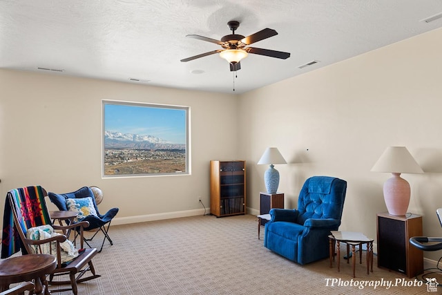 living area with ceiling fan, light colored carpet, and a textured ceiling