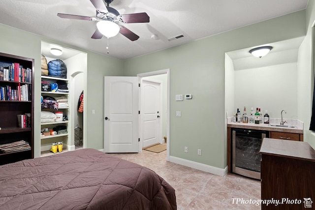 bedroom with indoor wet bar, wine cooler, and ceiling fan