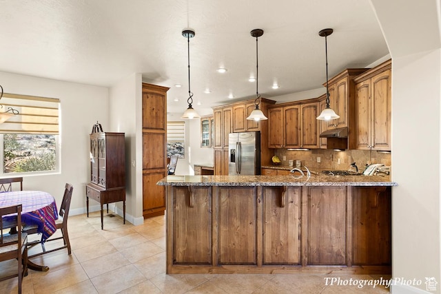 kitchen featuring stone countertops, decorative light fixtures, backsplash, kitchen peninsula, and stainless steel refrigerator with ice dispenser
