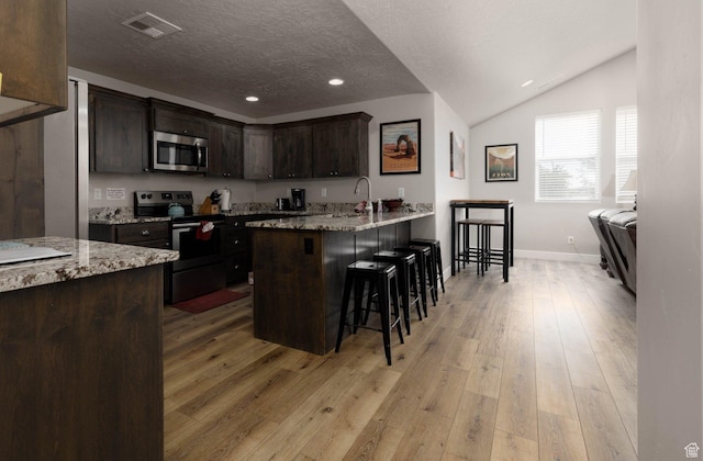 717 S 775 W, Hurricane, UT 84737 - kitchen with appliances with stainless steel finishes, a breakfast bar area, light stone counters, dark brown cabinets, and light hardwood / wood-style flooring