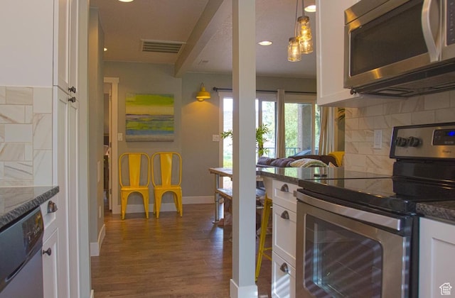 kitchen featuring appliances with stainless steel finishes, pendant lighting, white cabinetry, dark stone counters, and dark wood-type flooring