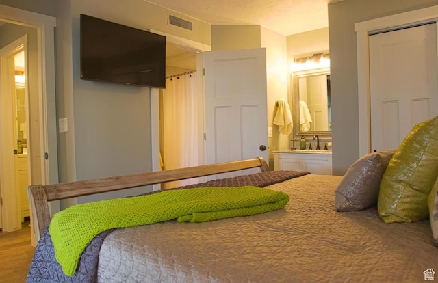 bedroom featuring wood-type flooring, connected bathroom, sink, and a textured ceiling