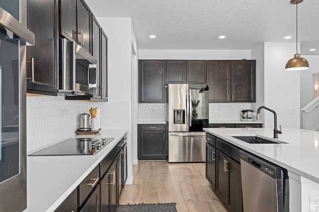 kitchen featuring sink, light wood-type flooring, pendant lighting, stainless steel appliances, and decorative backsplash