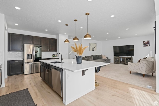 kitchen featuring appliances with stainless steel finishes, a breakfast bar, pendant lighting, sink, and a center island with sink