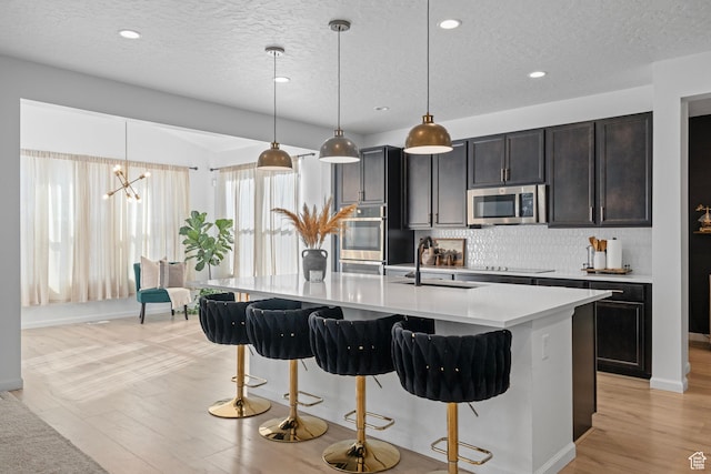 kitchen featuring sink, hanging light fixtures, stainless steel appliances, a kitchen island with sink, and decorative backsplash