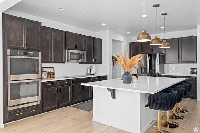 kitchen with appliances with stainless steel finishes, pendant lighting, an island with sink, a kitchen bar, and dark brown cabinetry
