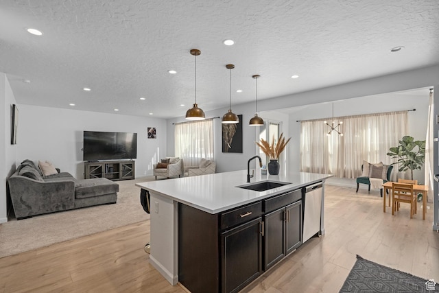 kitchen with sink, hanging light fixtures, stainless steel dishwasher, an island with sink, and light hardwood / wood-style floors